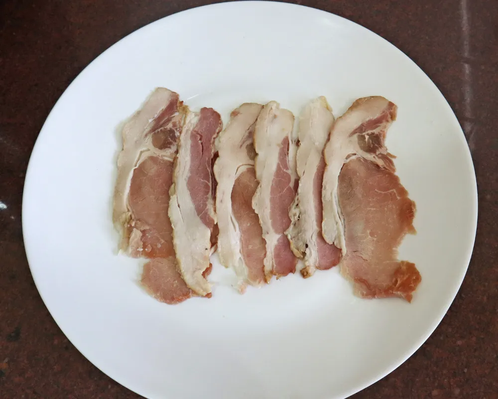 Raw bacon strips fanned out on a white plate before going into the air fryer