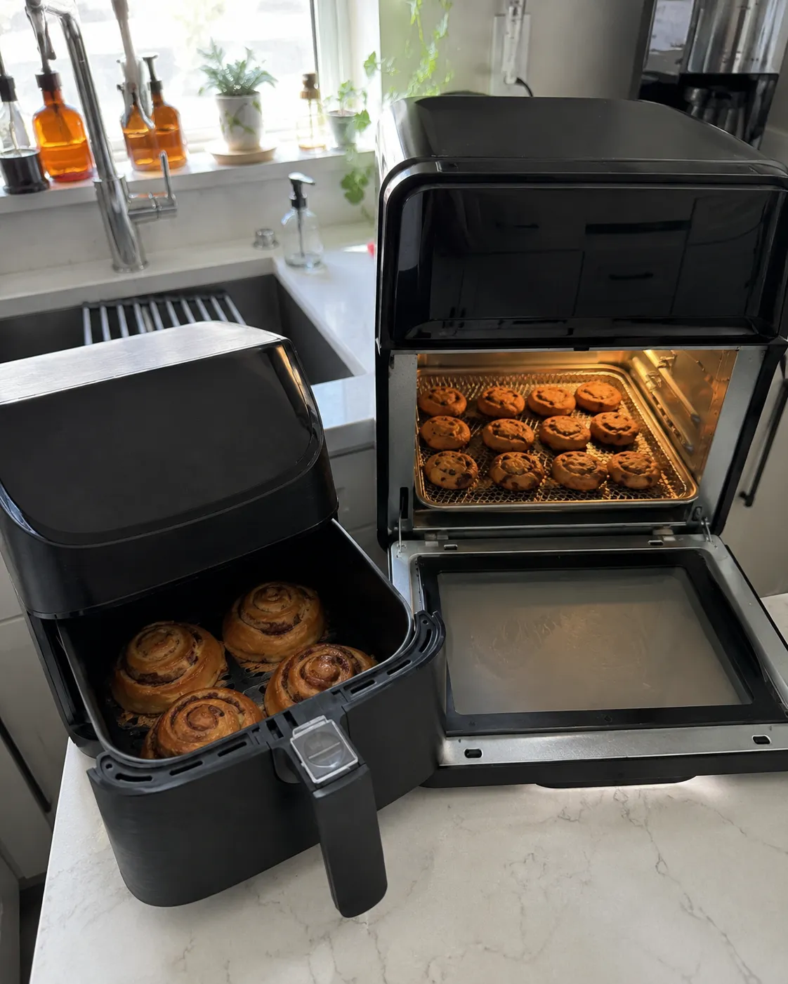 Cinnamon rolls baking in a basket air fryer beside a full tray of cinnamon rolls in an oven-style air fryer