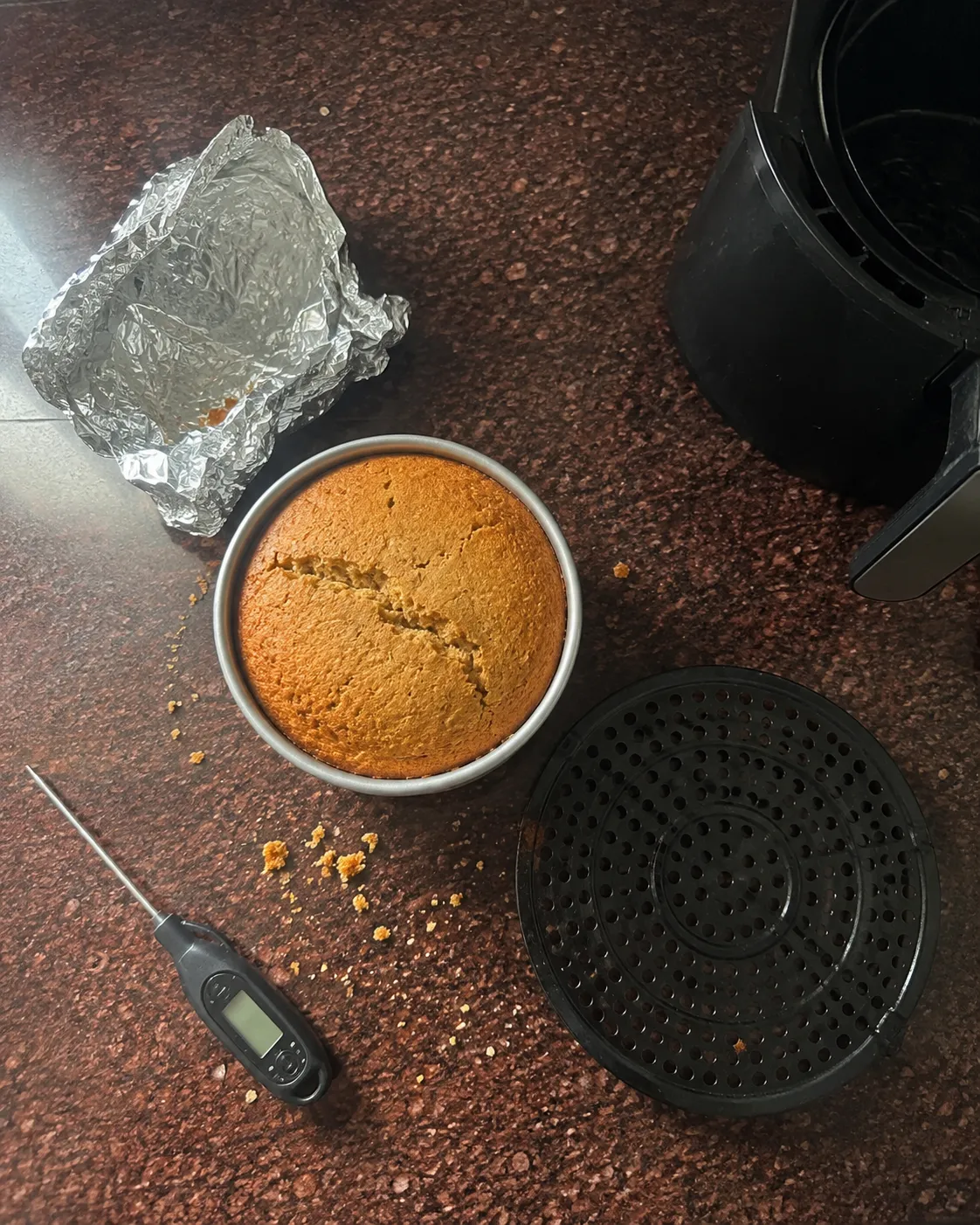 A cake tin, used foil, a digital thermometer and an air fryer crisper plate laid out on a kitchen counter