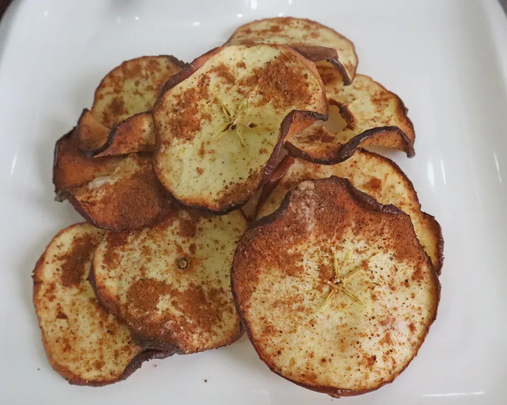 Crisp air fryer apple chips dusted with cinnamon on a white plate
