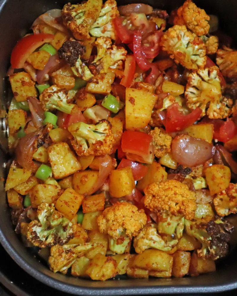 Cooked aloo gobi in an air fryer basket with browned cauliflower florets and golden potato in a single layer