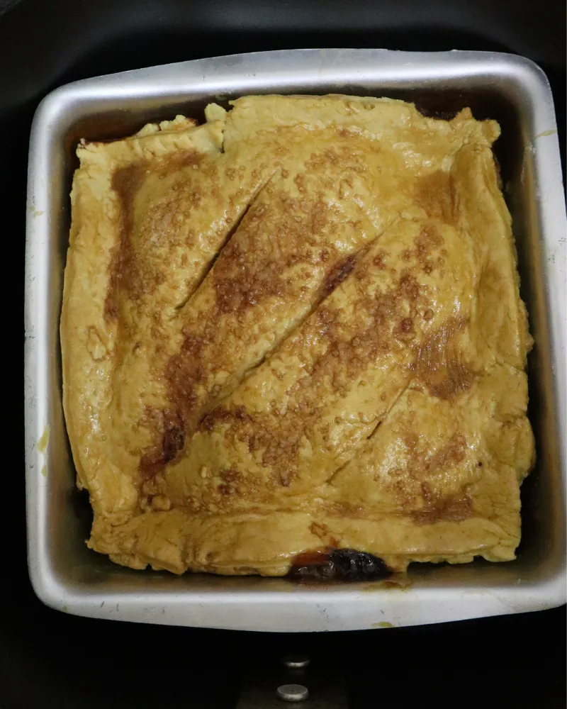 A baked air fryer apple pie in a square metal pan seen from above in the basket