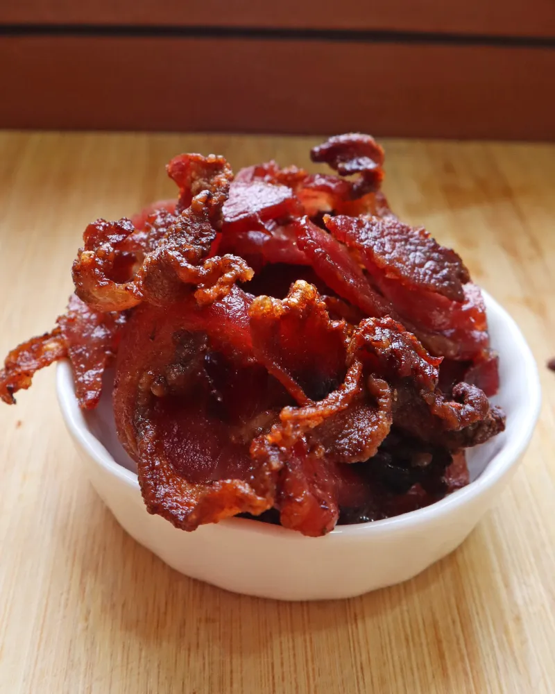 Crispy air fryer bacon piled in a white bowl on a wooden board