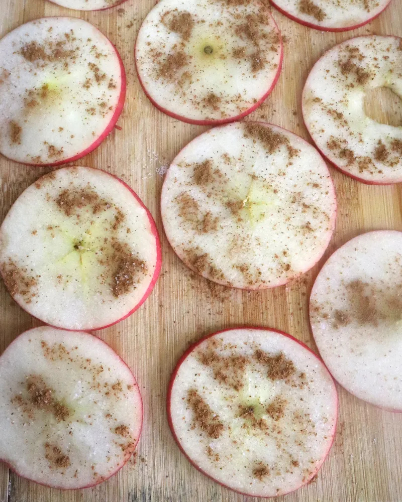Raw apple rings dusted with ground cinnamon laid out on a bamboo board