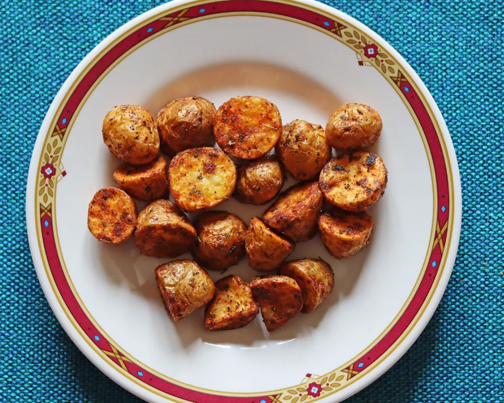 Halved and quartered air fryer baby potatoes served cut side up on a rimmed plate, each face deep golden brown