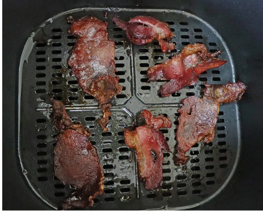 Six cooked bacon strips shrunk and spaced apart on an air fryer basket floor