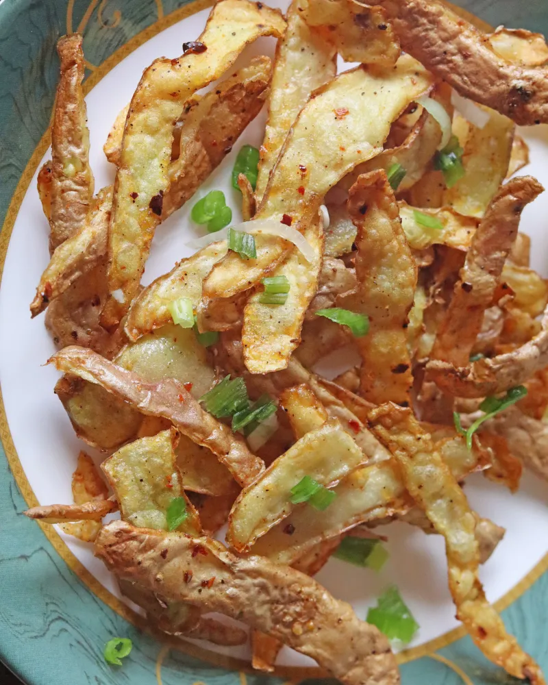 Crispy golden air fryer potato peels on a plate with scallions and chili flakes
