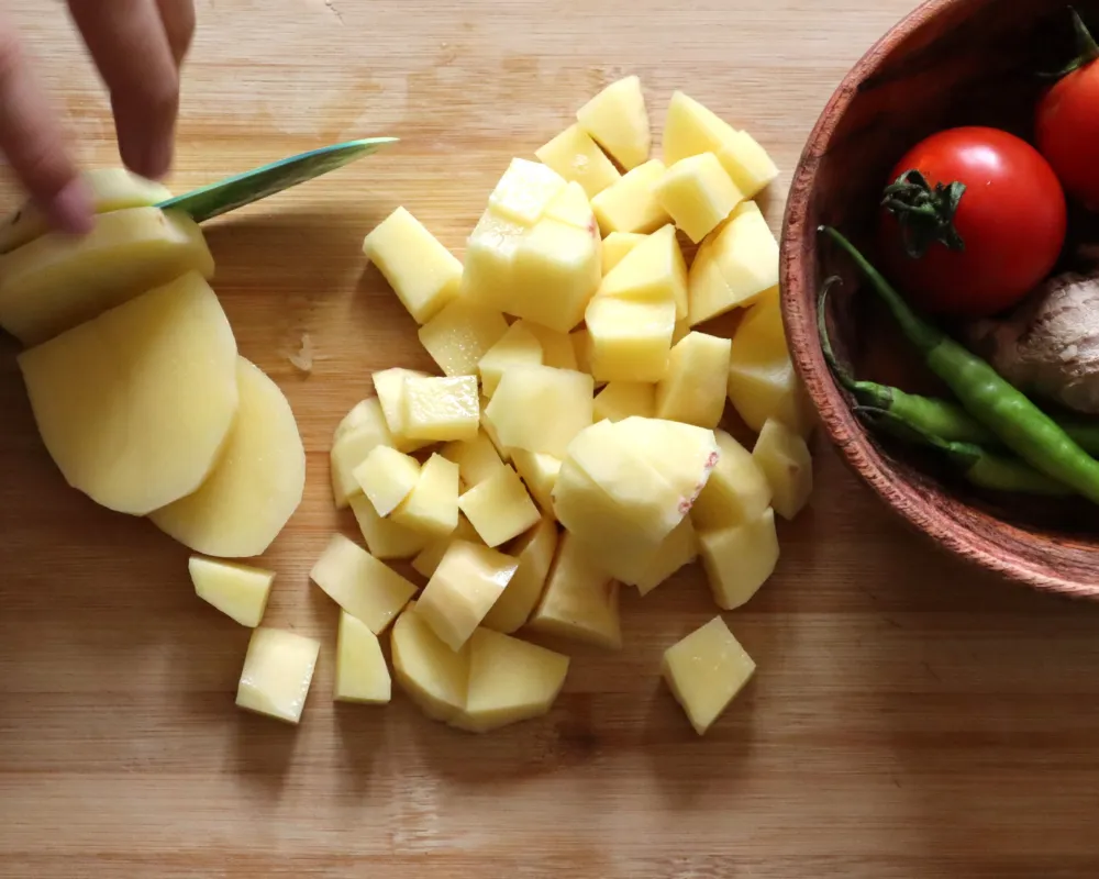 Peeled potatoes being cut into half inch cubes on a wooden board