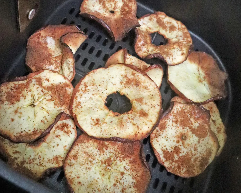 Close view of browned cinnamon dusted apple chips in an air fryer basket