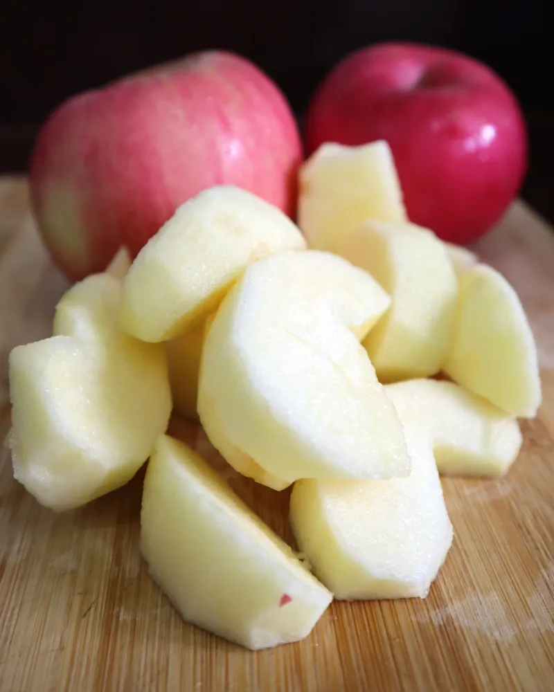Peeled apple pieces cut on a wooden board with two whole red apples behind them