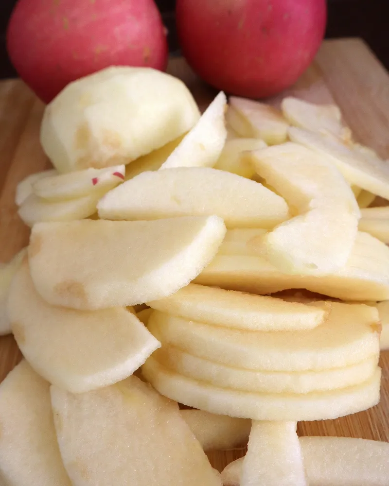 Peeled apple slices on a wooden board with whole red apples behind them