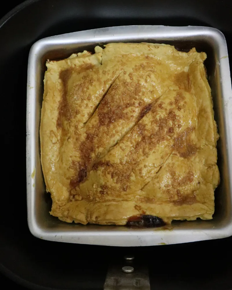 A baked apple pie in its metal pan inside an air fryer basket