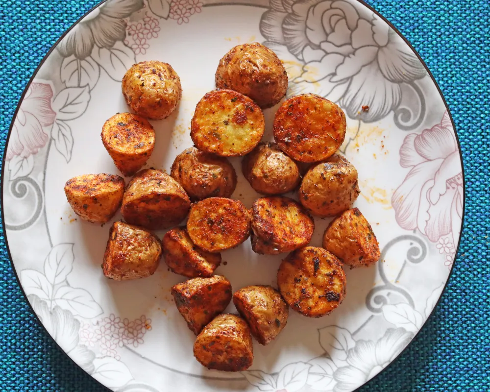 Finished air fryer baby potatoes on a floral plate, cut faces up and flecked with herbs and paprika
