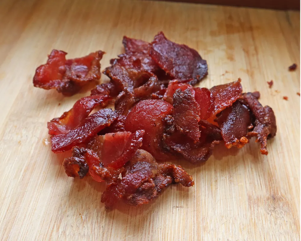 Crisp air fryer bacon broken into pieces on a wooden cutting board