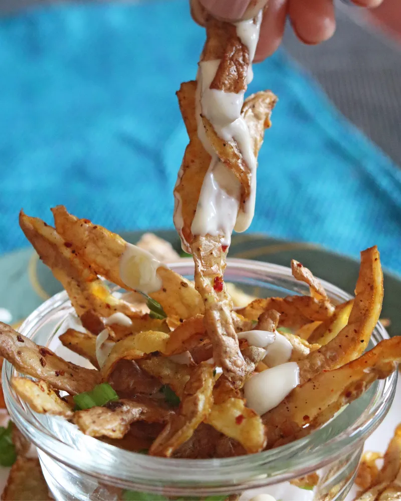 A hand dipping a crispy potato peel into a bowl of white dip