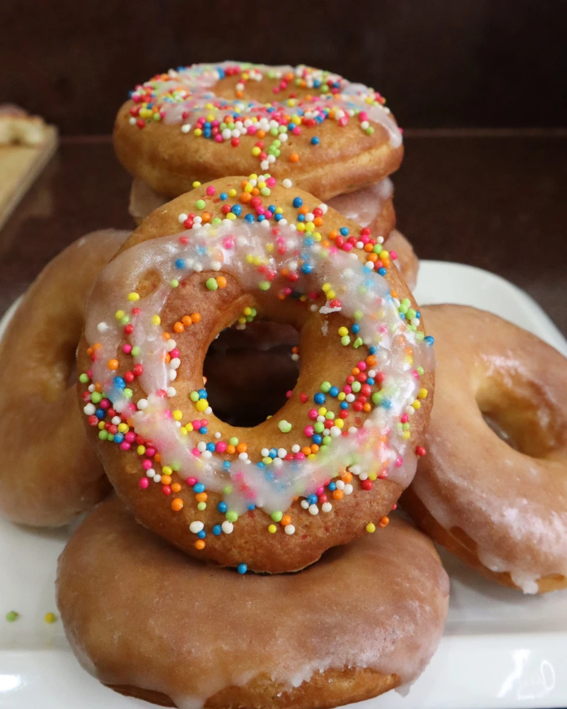 A close-up of a stack of vegan air fryer donuts with white glaze and rainbow sprinkles