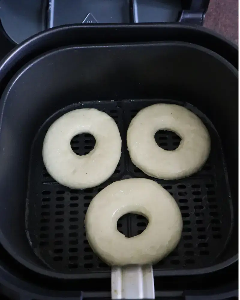 Three raw vegan donut rings spaced apart in a black air fryer basket