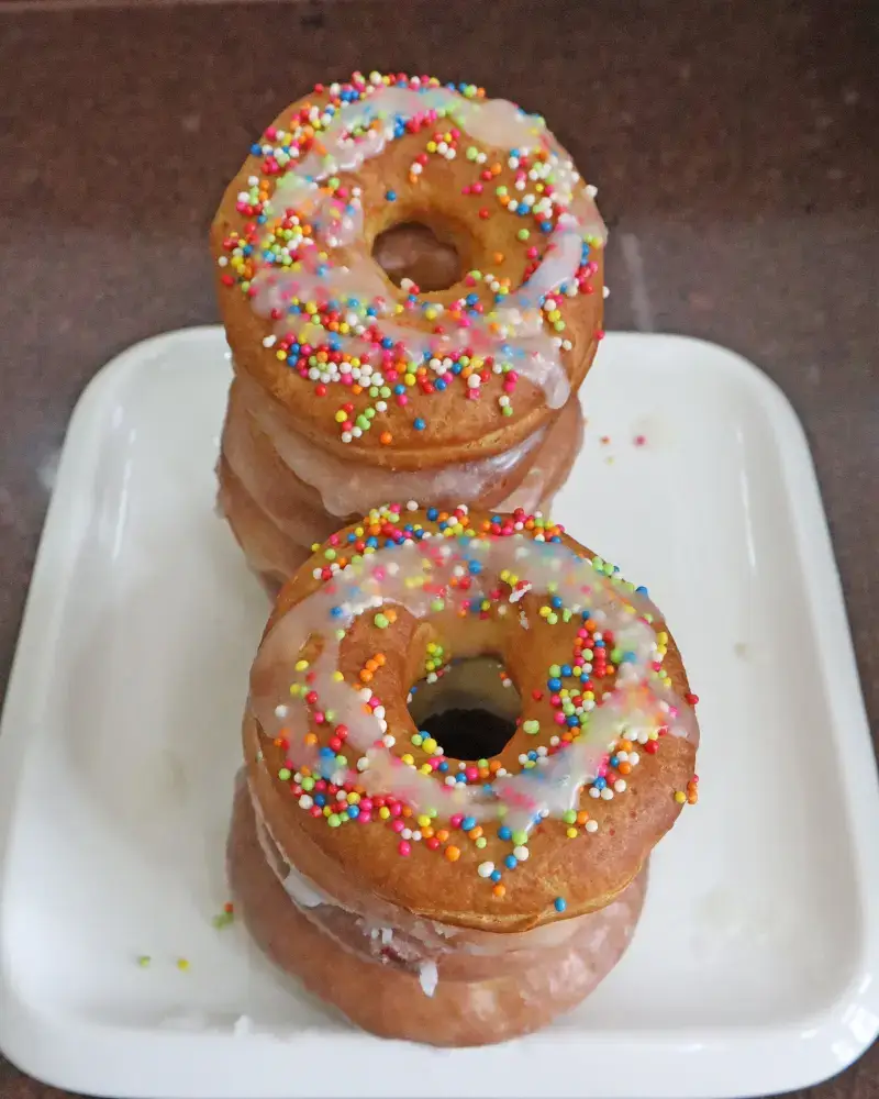 Two stacks of glazed vegan air fryer donuts topped with rainbow sprinkles on a white plate