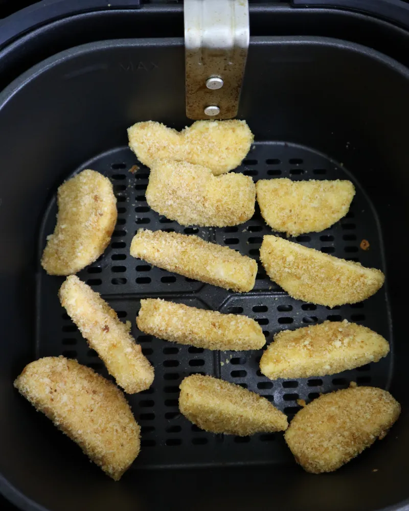 Breaded apple pieces arranged in a single layer in an air fryer basket before cooking