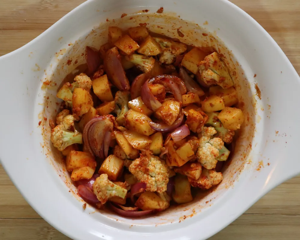 Raw potato, cauliflower and sliced onion tossed in a red-orange spice paste in a white bowl