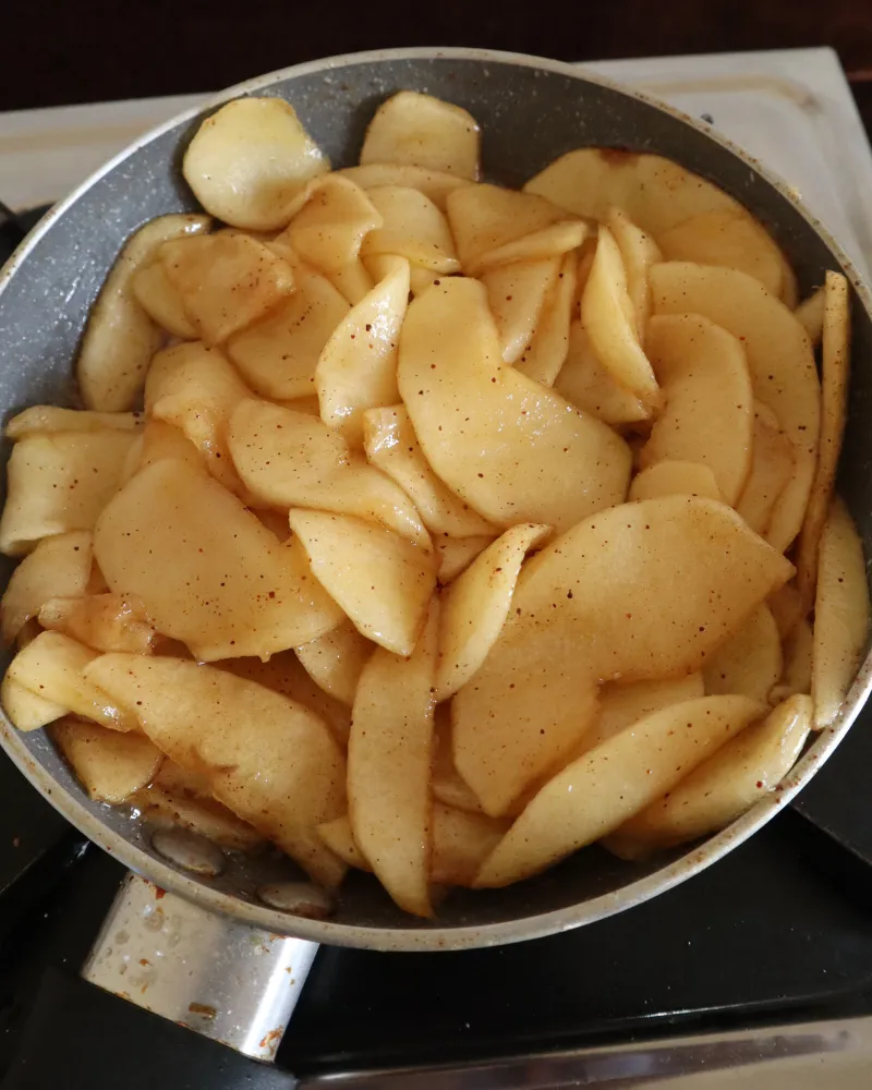 Apple slices cooking down with cinnamon and butter in a skillet on the stove