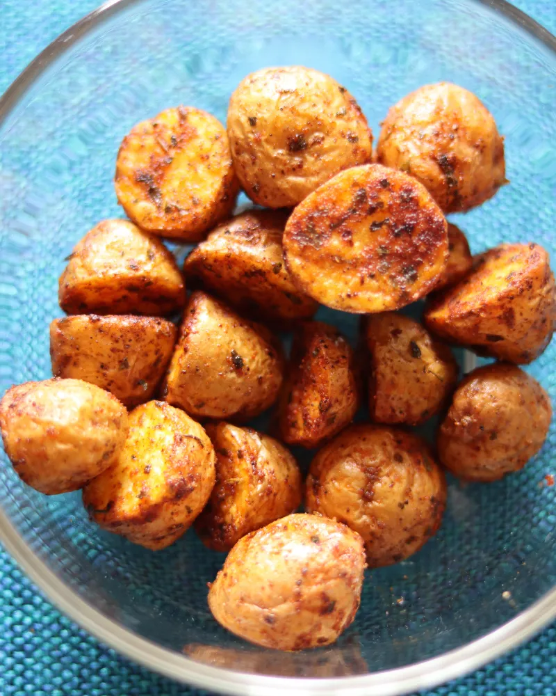 A glass bowl of finished air fryer baby potatoes piled cut side up, the faces deeply browned and the skins matte