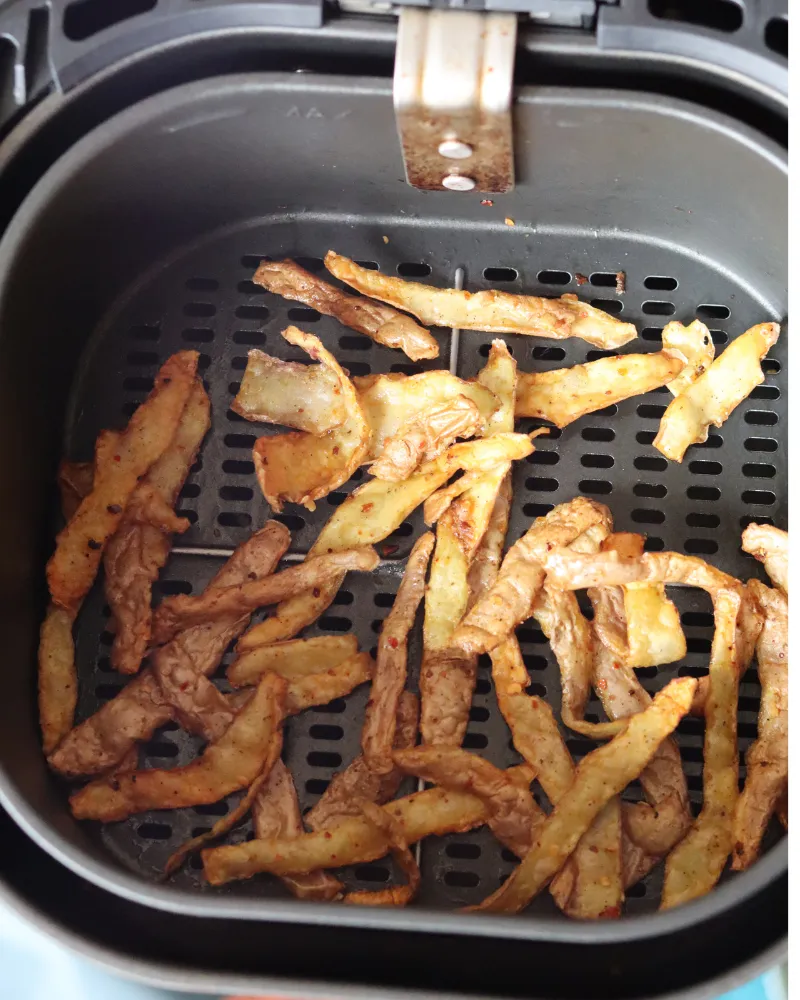 Cooked golden brown potato peels in an air fryer basket after crisping