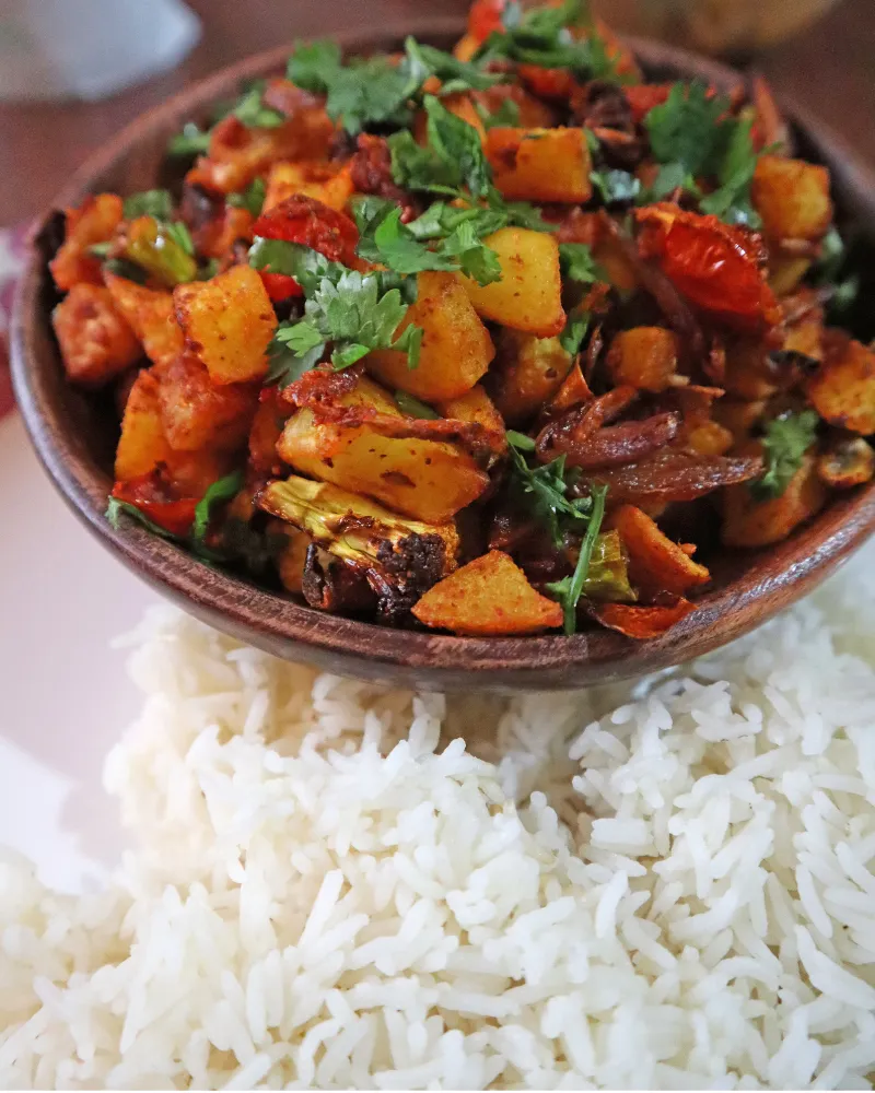 A bowl of air fryer aloo gobi topped with cilantro served beside a plate of steamed basmati rice