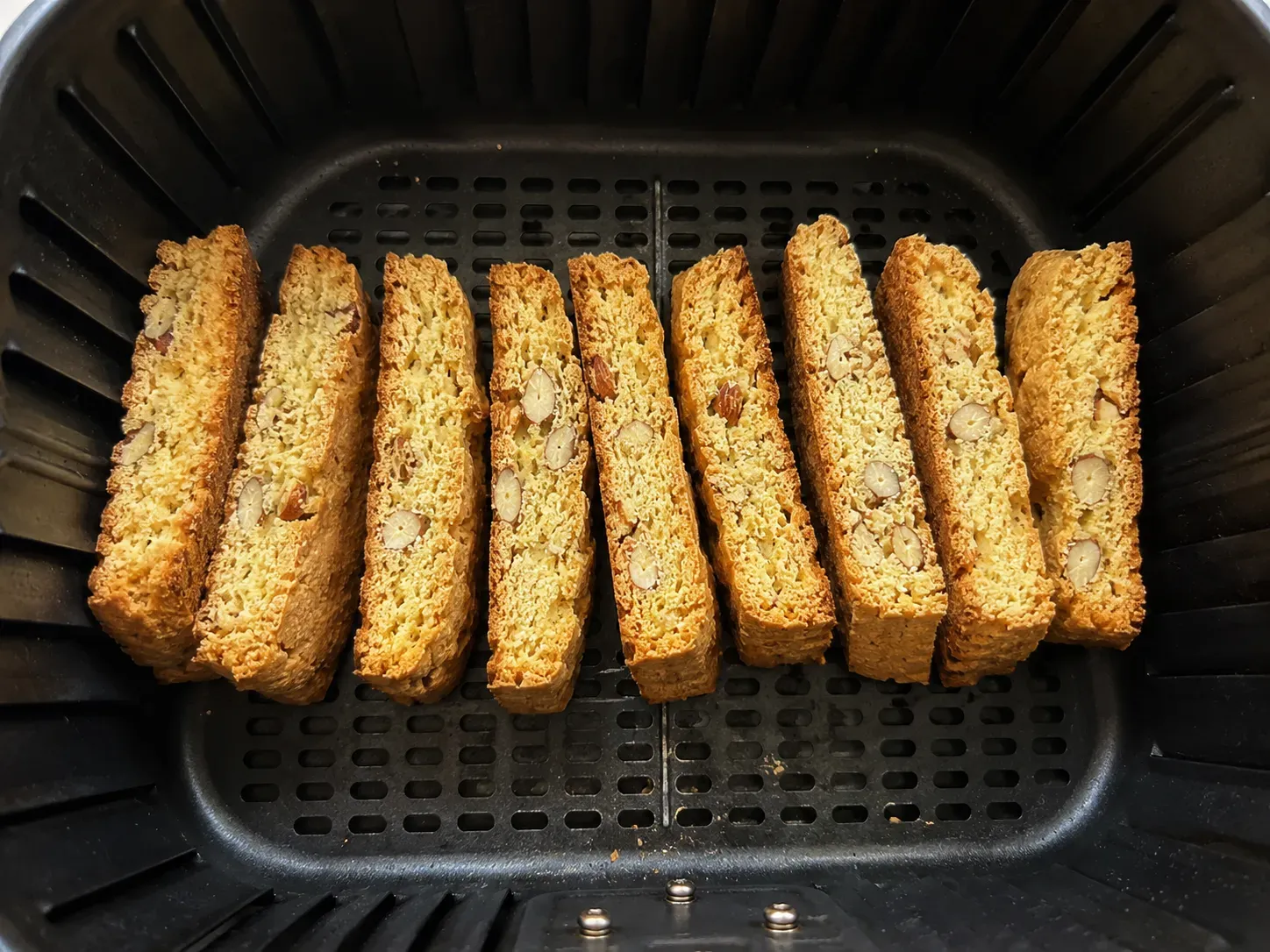 Nine biscotti slices standing upright on their edges in an air fryer basket