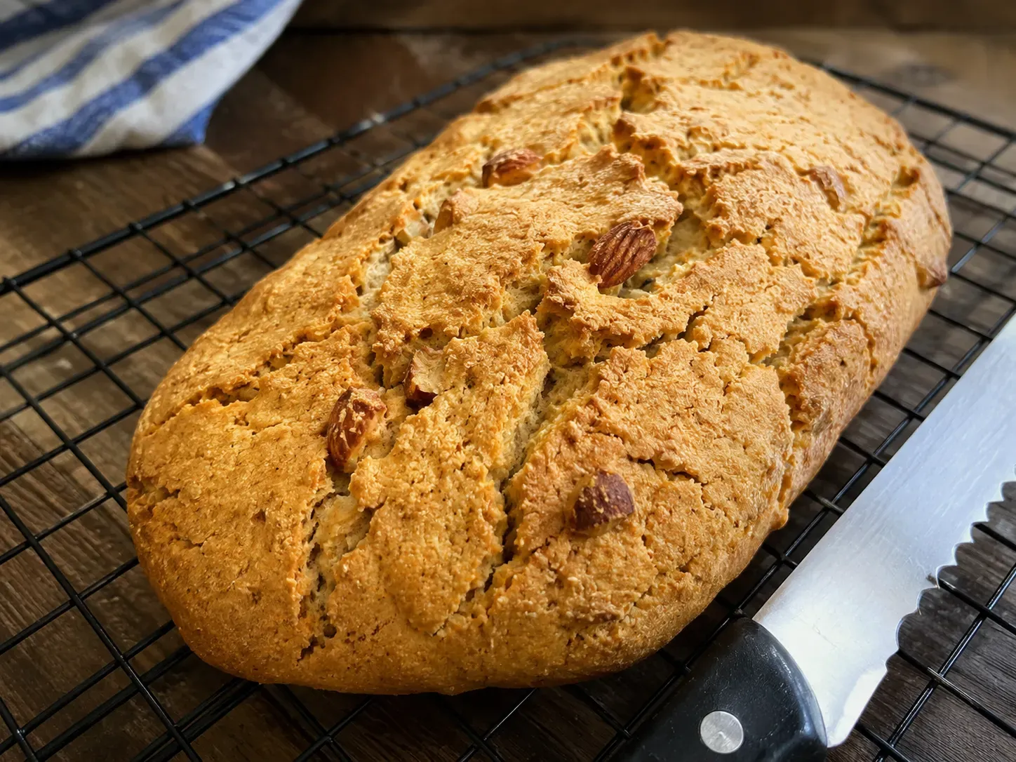 A baked almond biscotti log cooling on a wire rack with a serrated knife beside it
