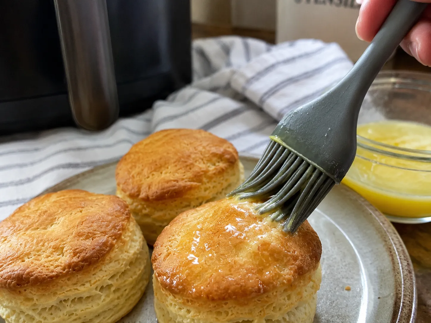 Melted butter being brushed over hot canned biscuits fresh from the air fryer