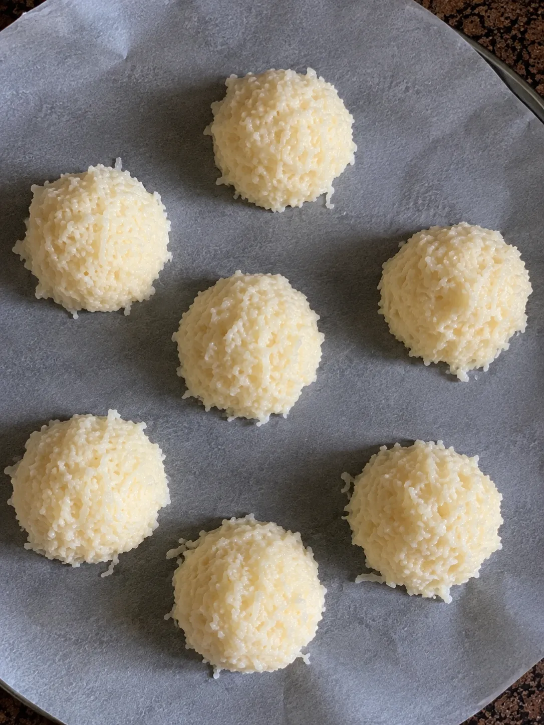 Seven scooped coconut macaroon mounds spaced on a parchment round ready for the air fryer