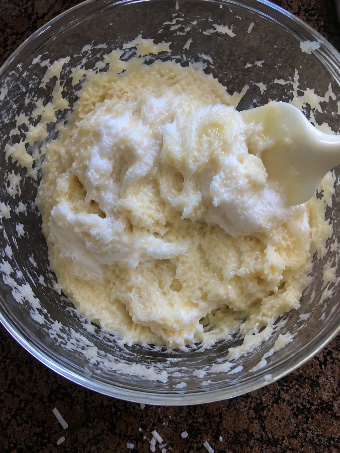 Whipped egg white being folded into a bowl of coconut and condensed milk with a spatula