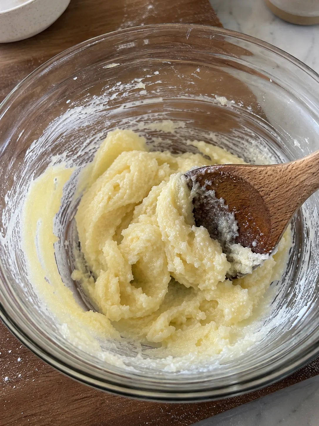 Butter and sugar creamed to a smooth pale mixture in a glass bowl with a wooden spoon