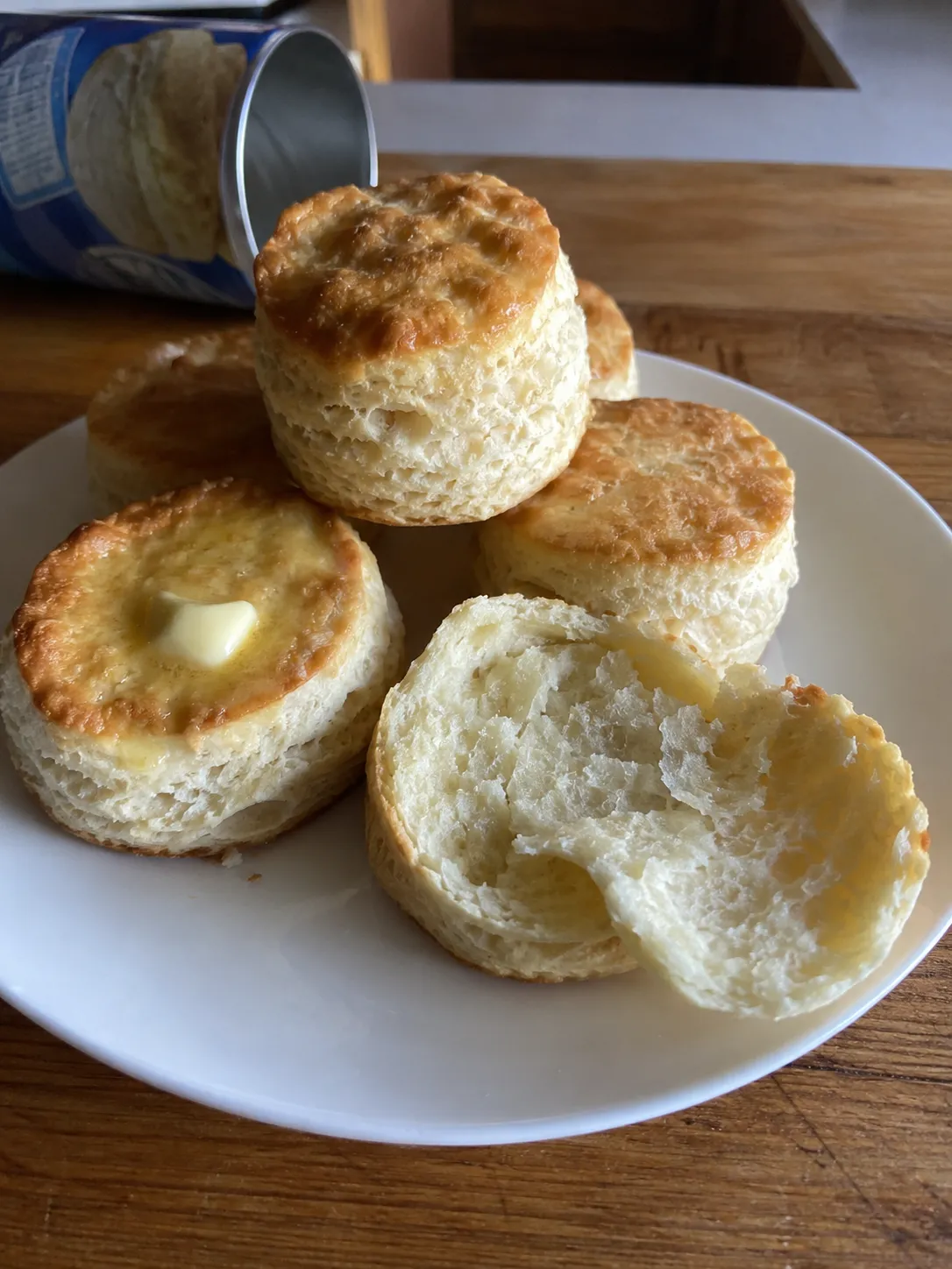 Air fryer canned biscuits on a plate, one torn open to show flaky layers, with butter melting on another