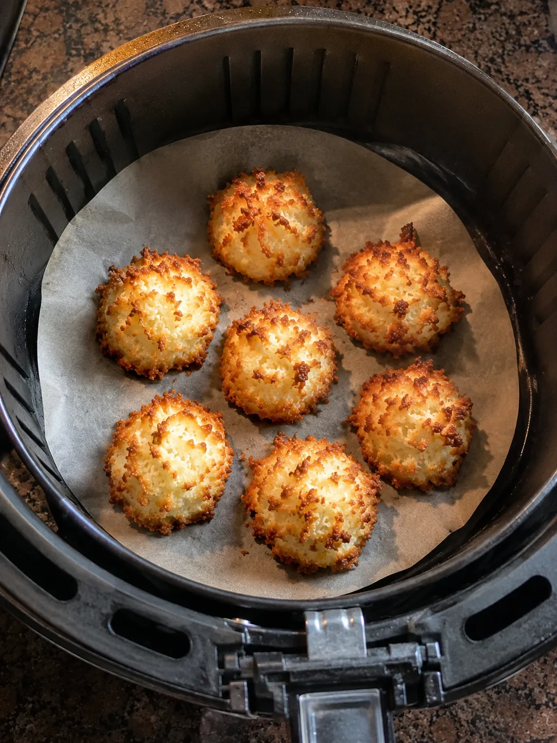 Seven golden baked coconut macaroons on parchment inside an air fryer basket
