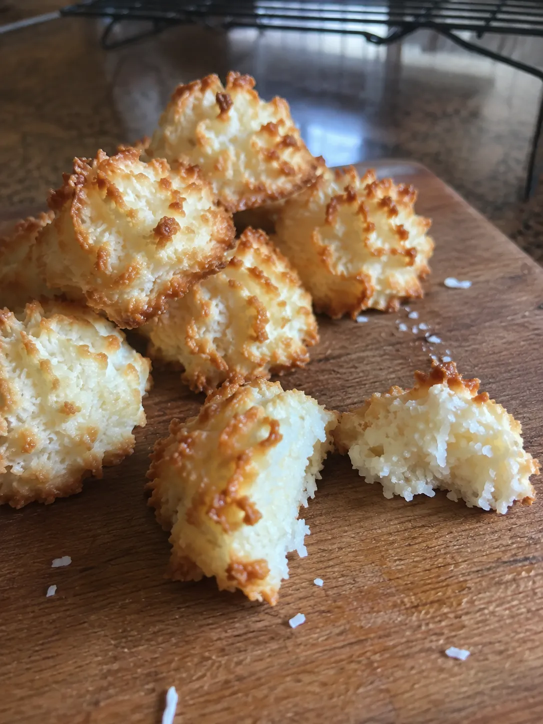 Air fryer coconut macaroons with deep gold tips on a wooden board, one broken open to show the chewy inside