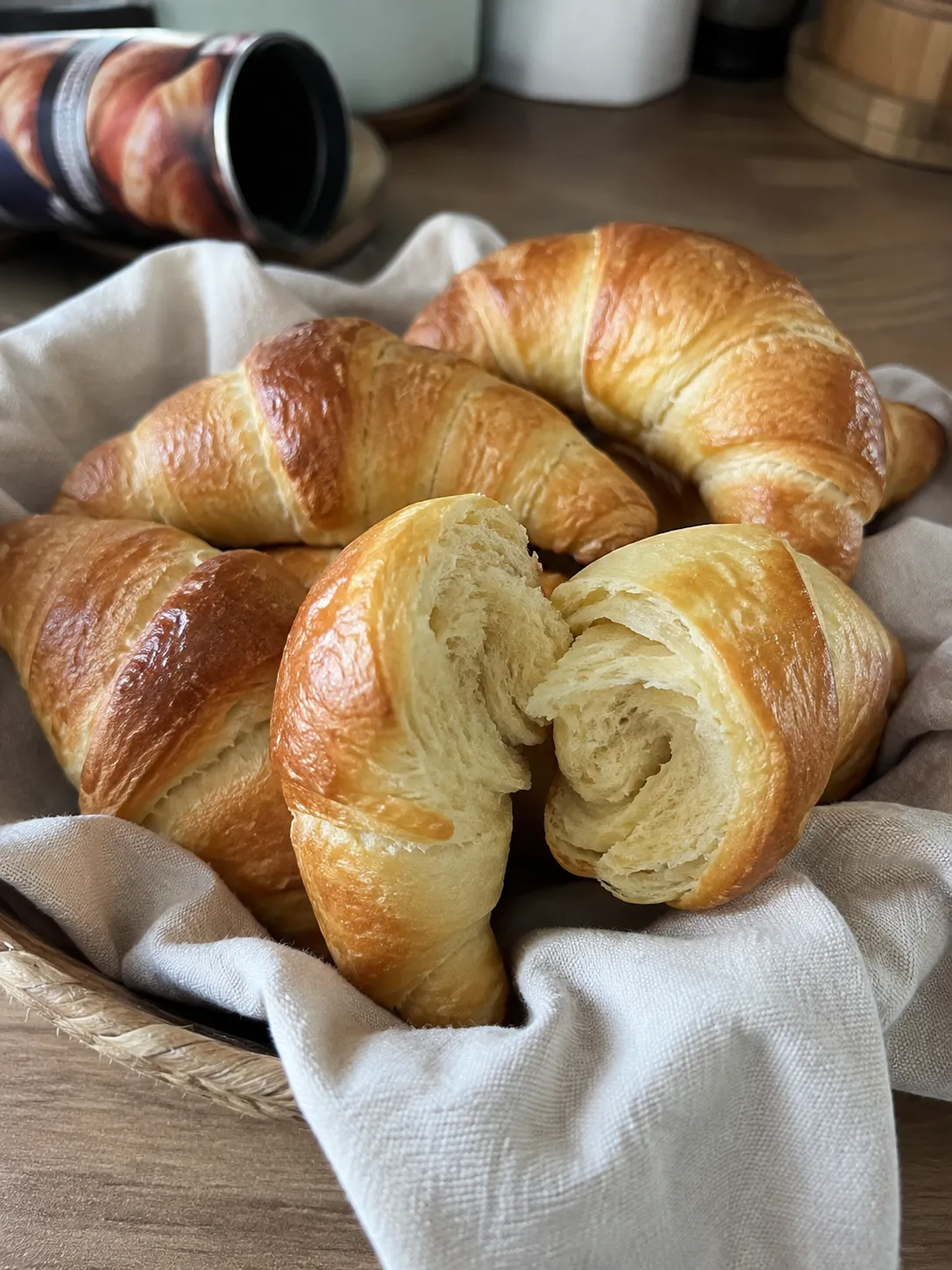 Golden air fryer crescent rolls in a cloth-lined basket, one torn open to show the soft spiral crumb