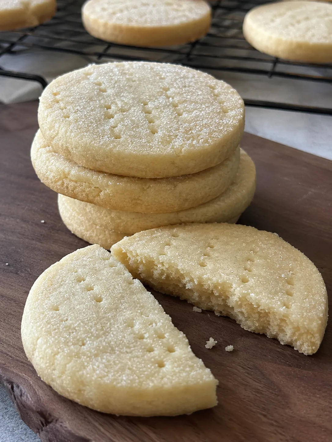 Stack of air fryer shortbread cookies on a wooden board with one snapped in half showing a sandy crumb