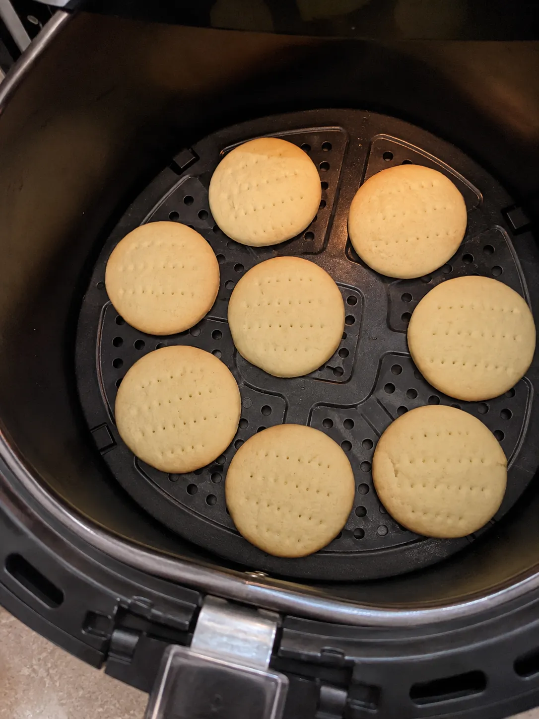 Eight docked shortbread cookies baked pale gold on the crisper plate of an air fryer basket