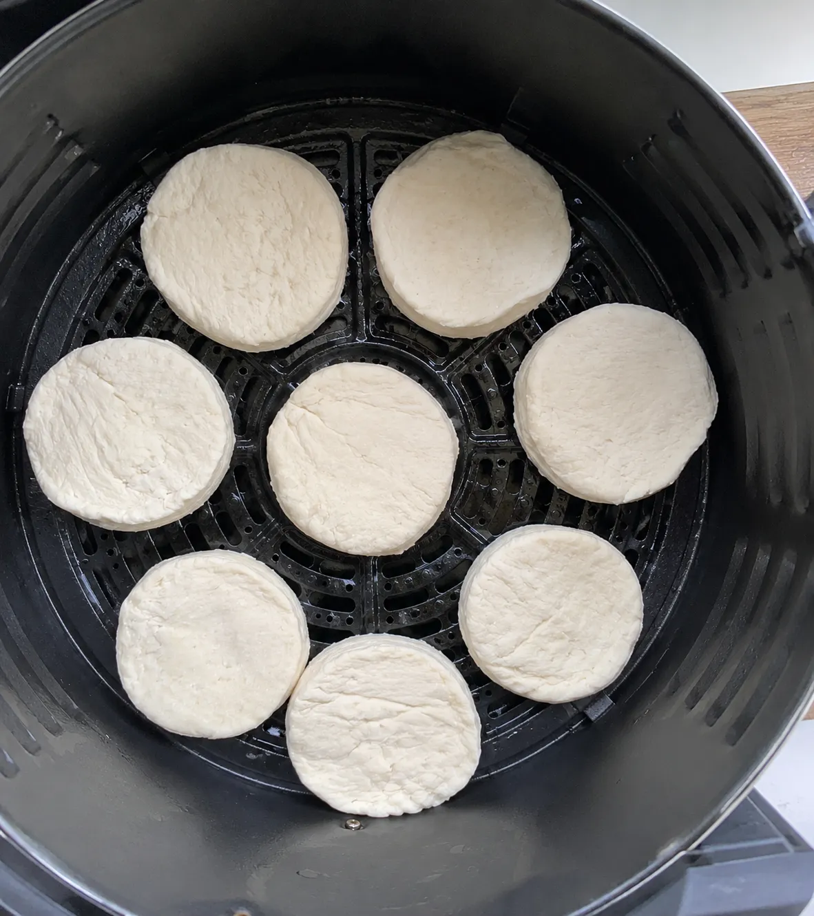 Eight raw canned biscuits spaced in a single layer on the floor of an air fryer basket