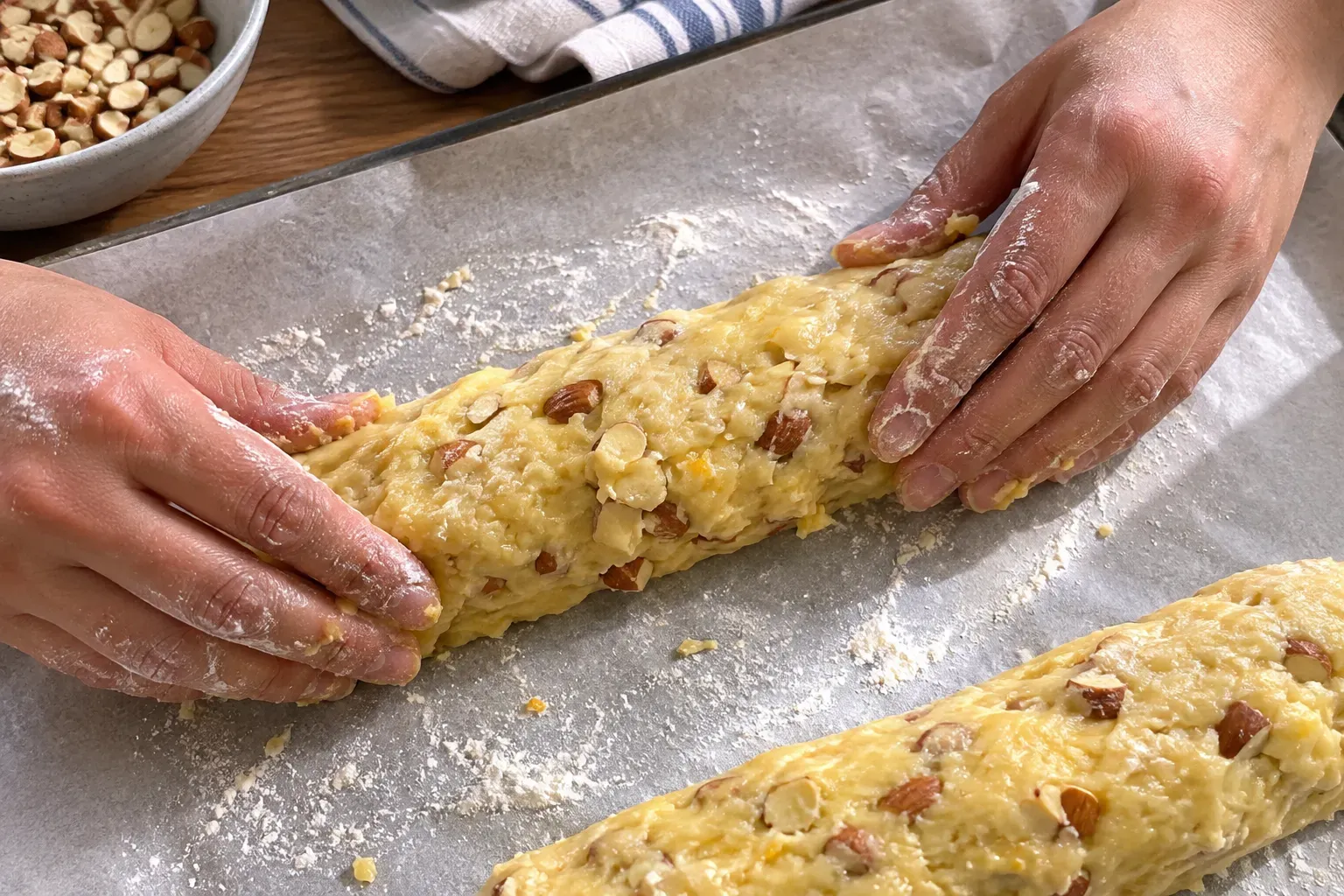 Shaping sticky almond biscotti dough into a log on floured parchment, with a second log alongside