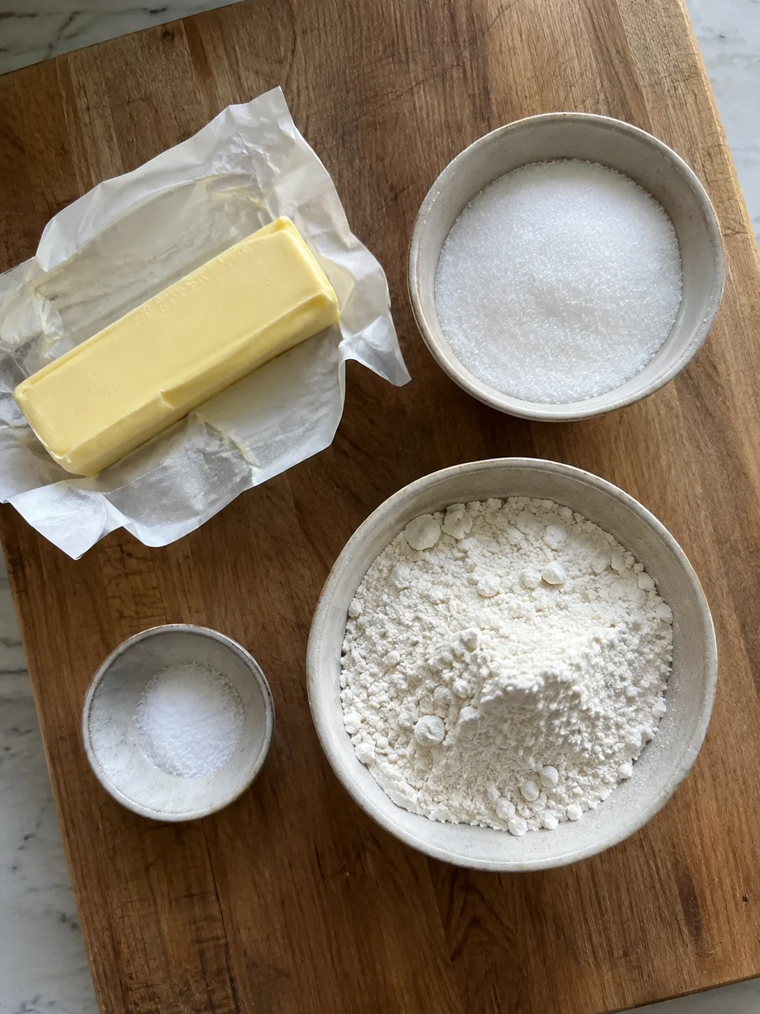 Butter, granulated sugar, flour and salt measured into bowls on a wooden board