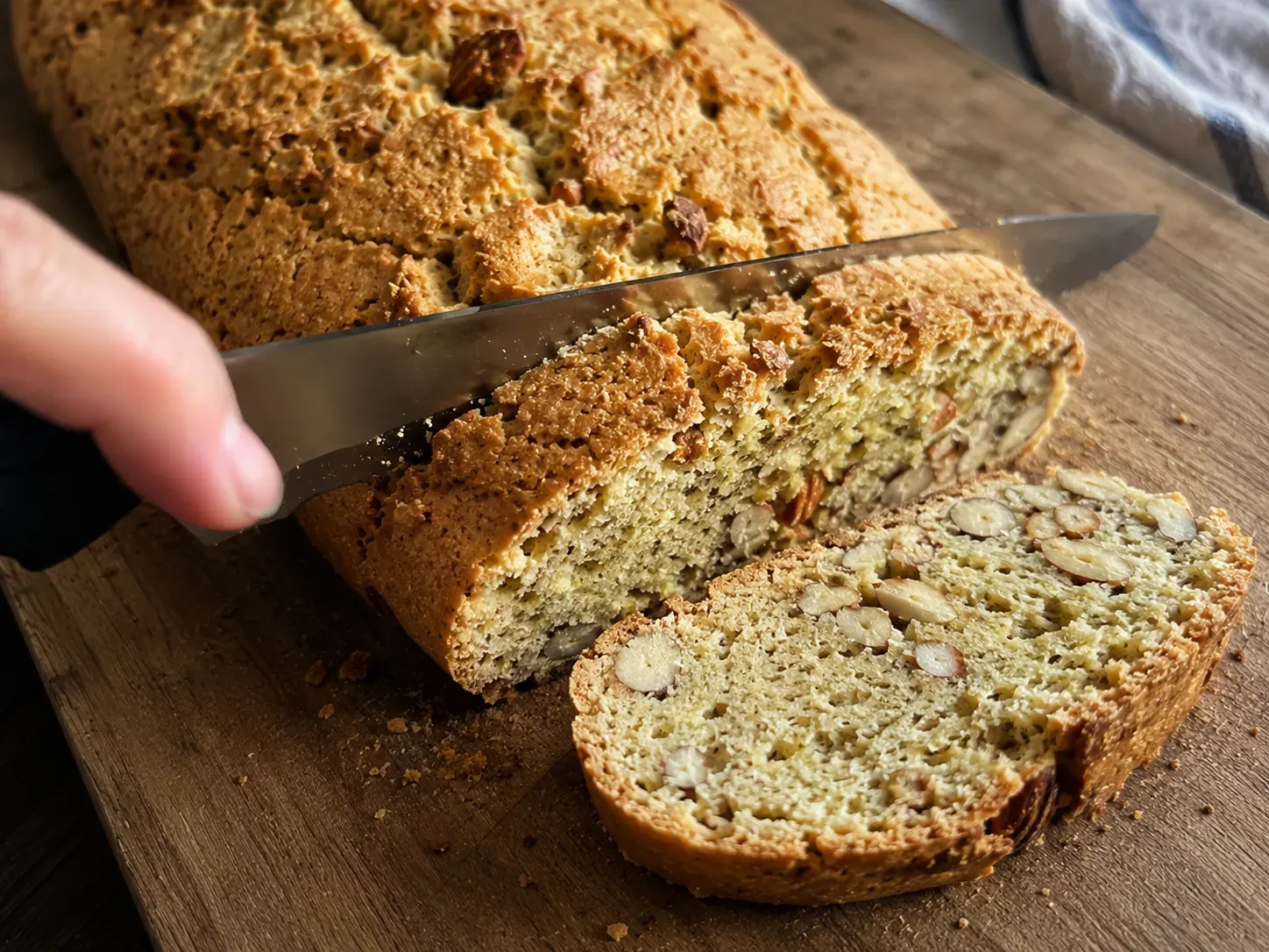 Cutting a warm biscotti log into diagonal slices with a serrated knife, showing the almond-studded crumb
