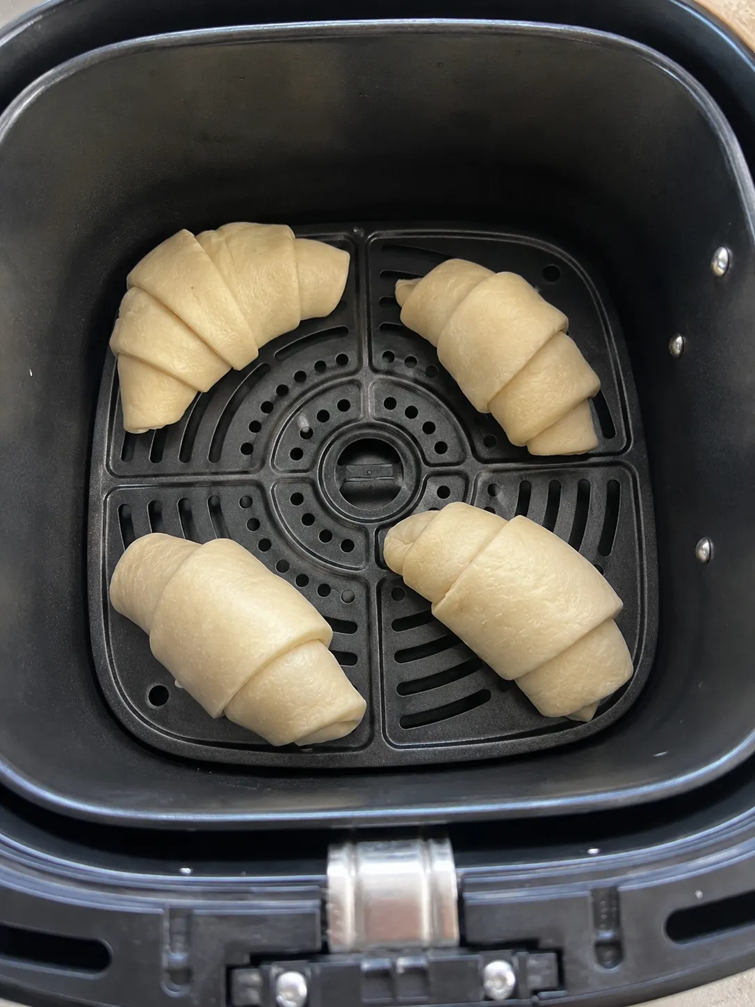 Four raw shaped crescent rolls spaced apart in an air fryer basket, each with its point tucked underneath