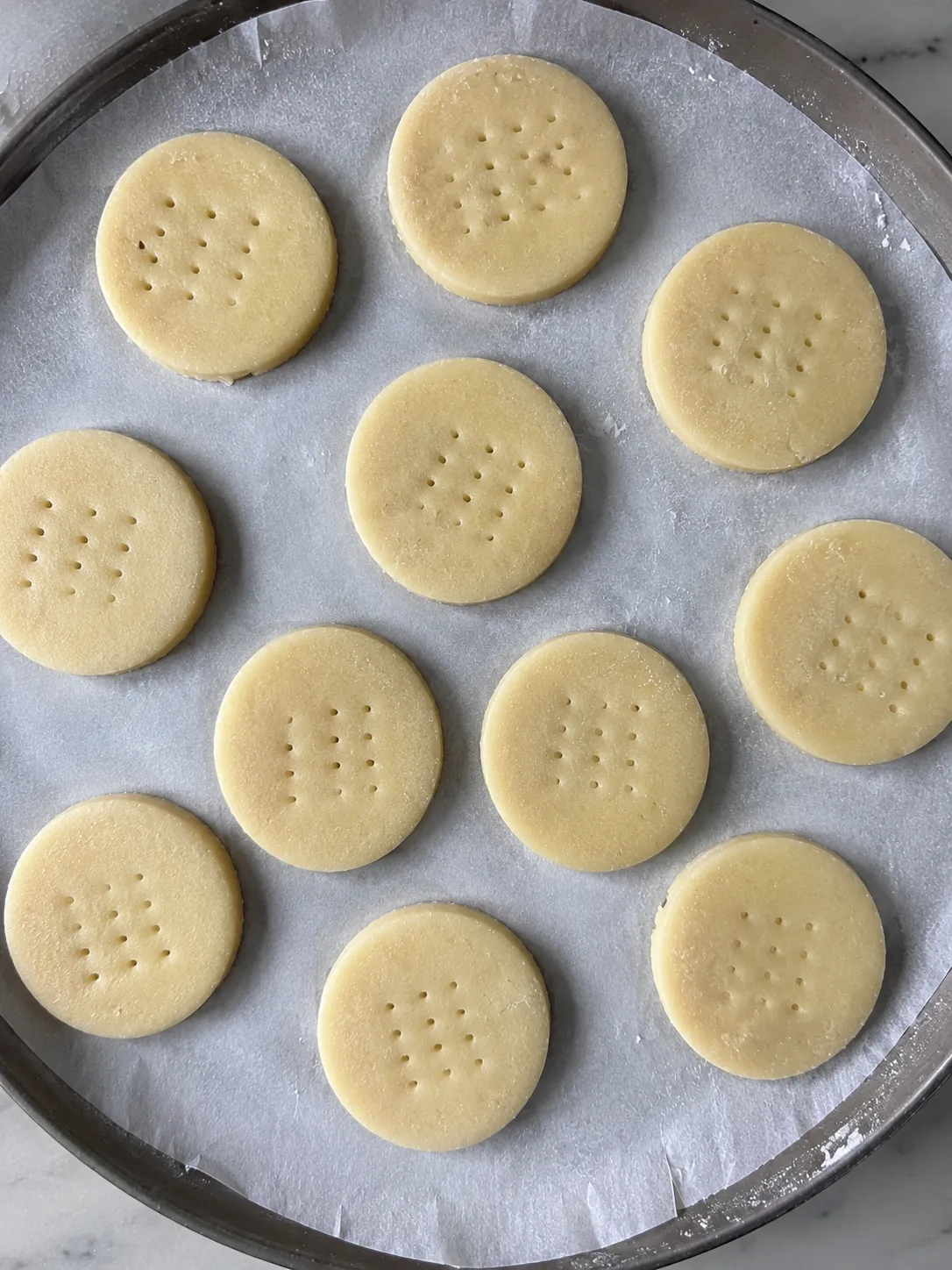 Eleven docked rounds of shortbread dough spaced on a parchment-lined tray before chilling