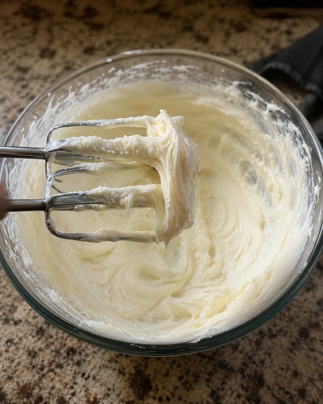 Beaters lifted from a glass bowl of cream cheese filling beaten completely smooth and glossy