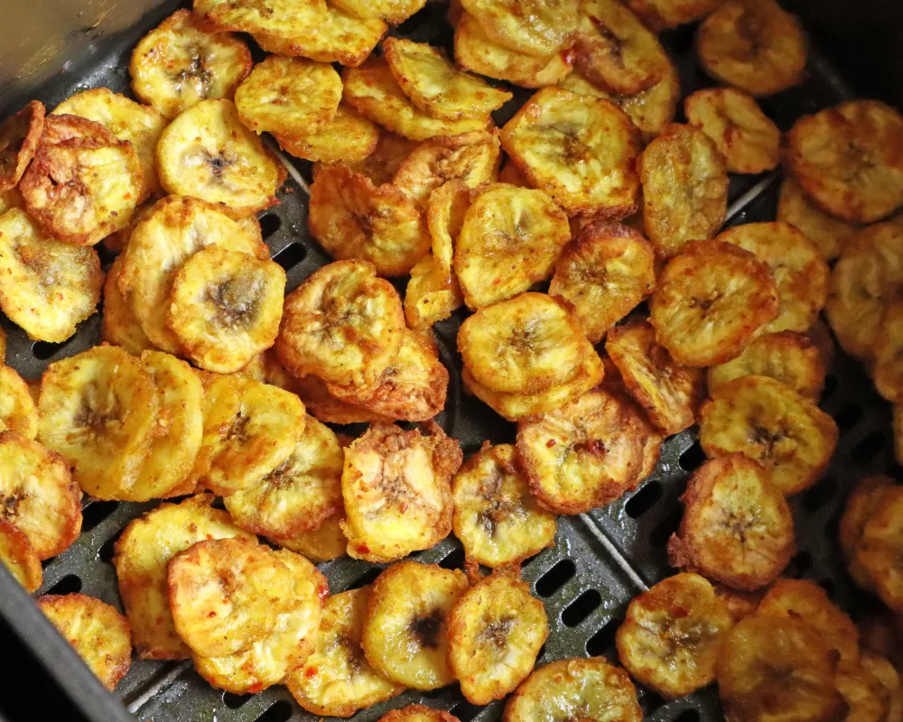 Cooked banana chips filling an air fryer basket, golden and flecked with chili