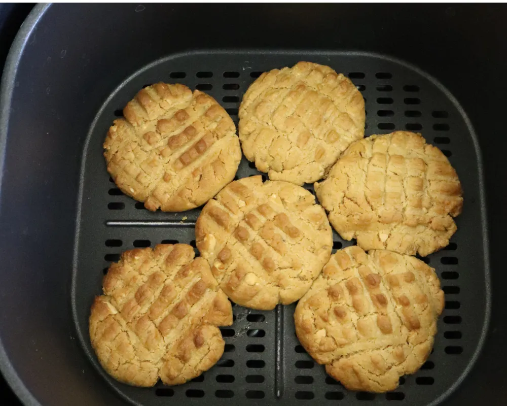 Six golden baked peanut butter cookies in an air fryer basket