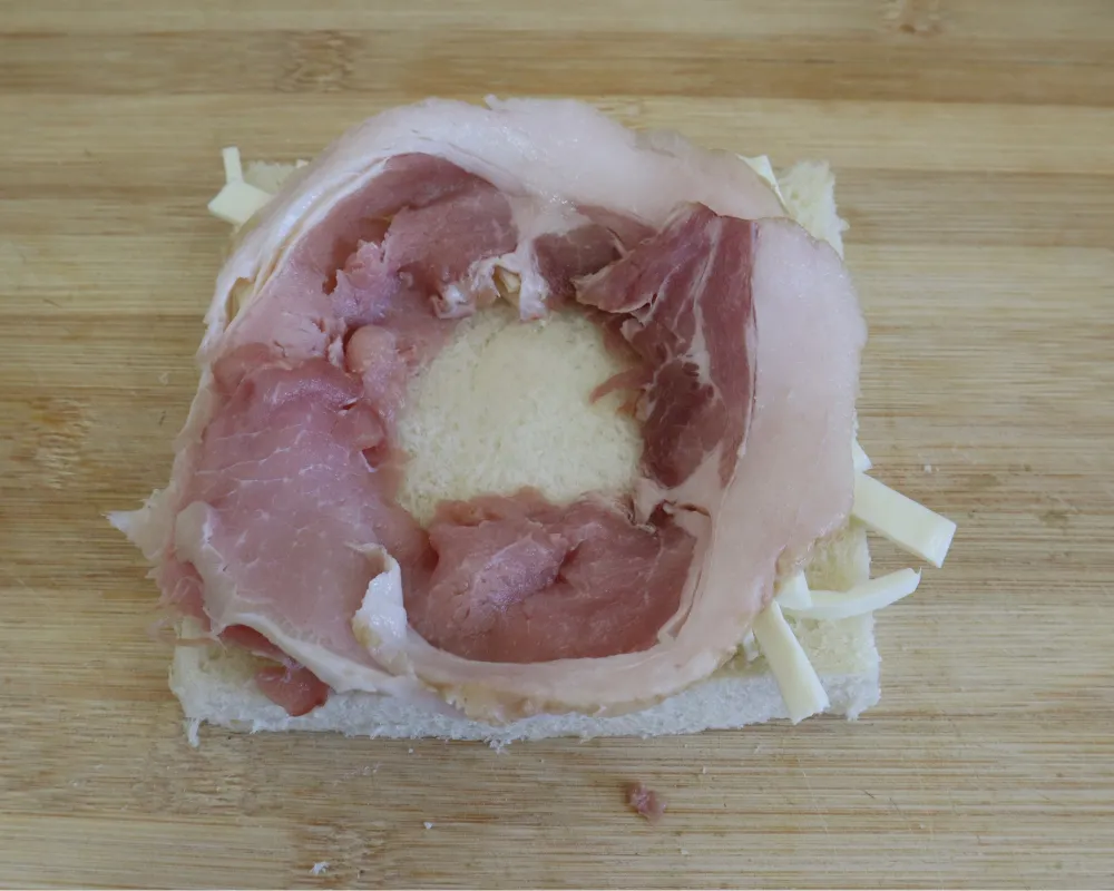 A rasher of bacon coiled into a ring on top of the cheese-lined bread slice